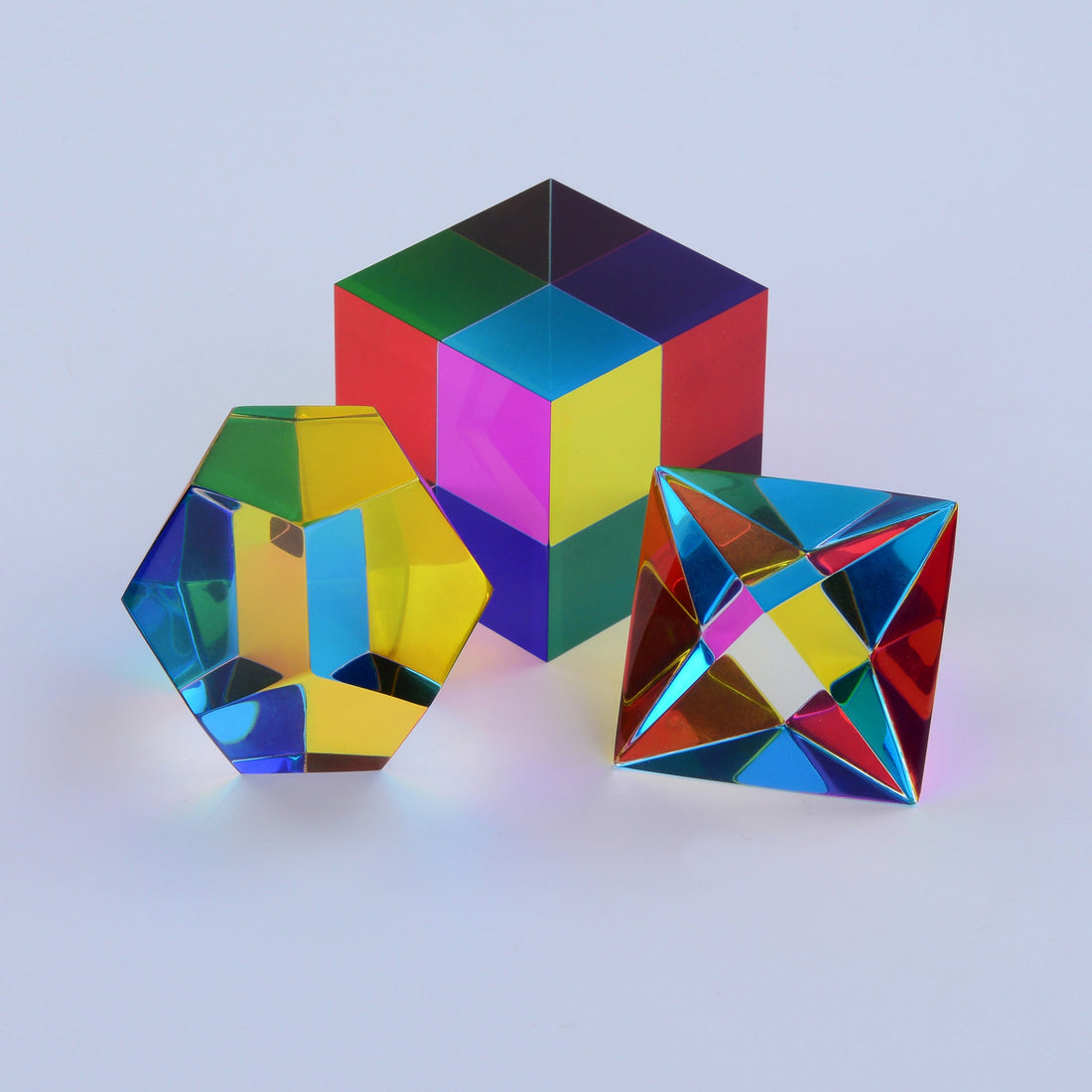 Three translucent CMY Platonic solids overlapping in sunlight, mixing cyan, magenta and yellow into new colours
