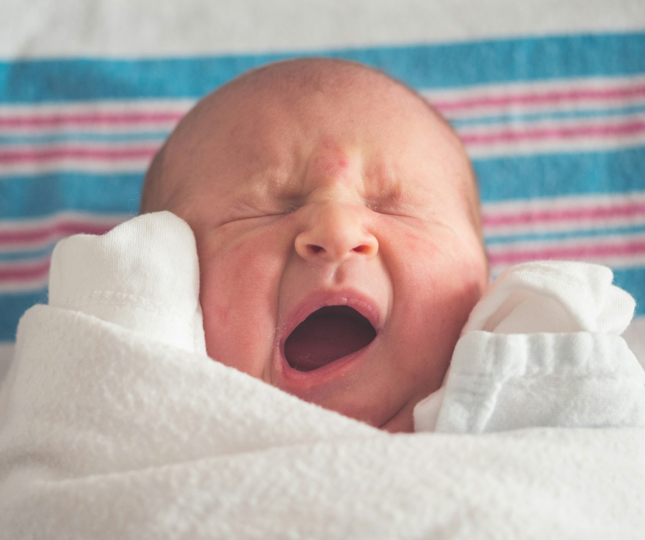 Newborn baby yawning, wrapped in a white blanket