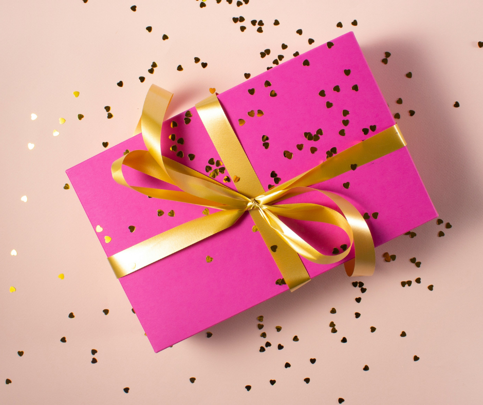 Pink gift box tied with gold ribbon on a pink background with confetti